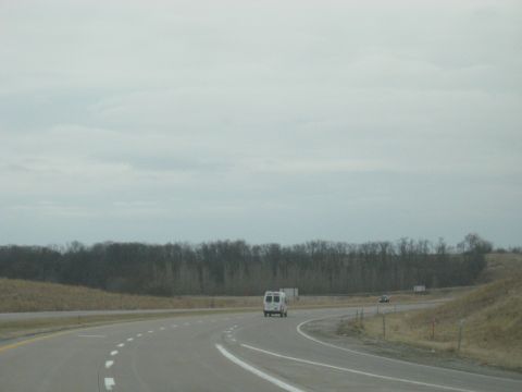 1978 Ford Bronco - A white van travels down a highway under a cloudy sky, with a dark car visible in the distance.