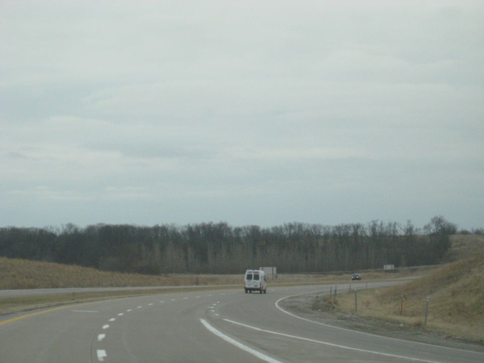 White van driving on a highway with trees in the background