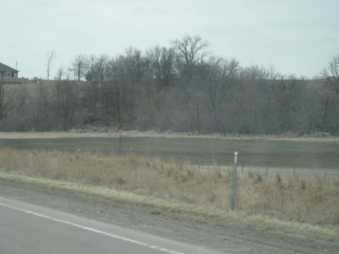 1978 Ford Bronco - A rural landscape unfolds with a distant house and a line of bare trees against a muted sky.