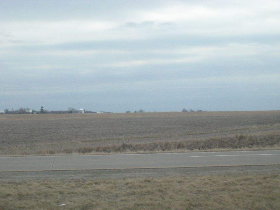 Farm buildings visible on the horizon across a barren field with a road in the foreground