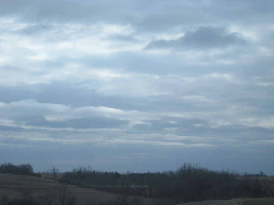 Overcast sky above a rural landscape with bare trees and fields