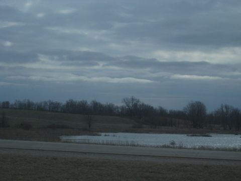 1978 Ford Bronco - A cloudy sky looms over a tranquil rural landscape with a small lake.