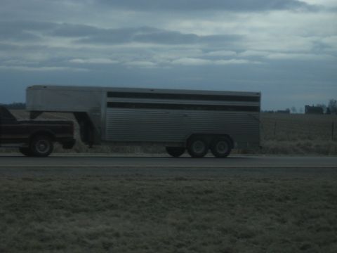 1978 Ford Bronco - A pickup truck tows a large gooseneck livestock trailer down a highway under a cloudy sky.