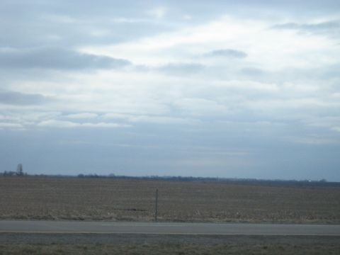1978 Ford Bronco - A desolate landscape unfolds with a paved road leading towards a barren field under an overcast sky.