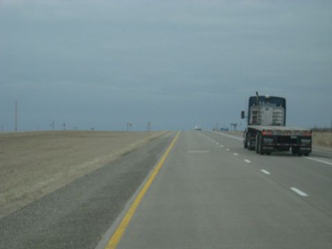 1978 Ford Bronco - A flatbed semi-truck travels down a highway under a cloudy sky.