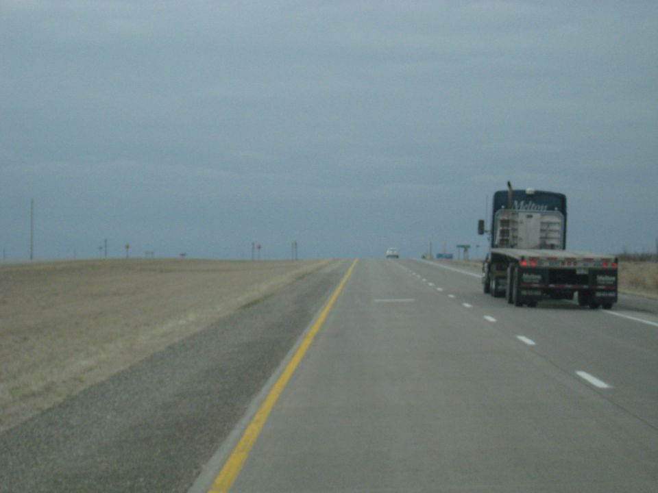 Flatbed semi-truck on highway with a white car in the distance