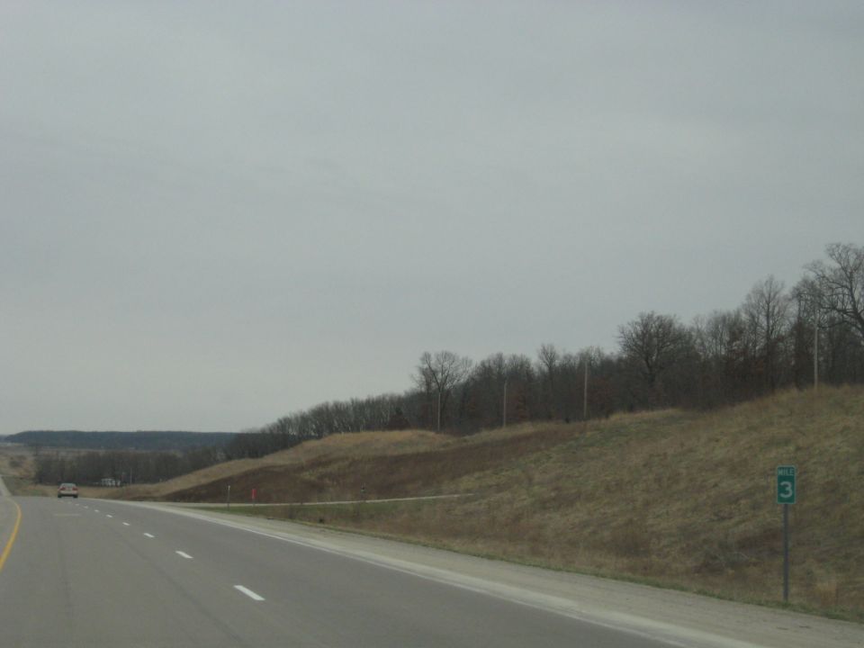 Car driving on a highway with a grassy embankment and trees under an overcast sky