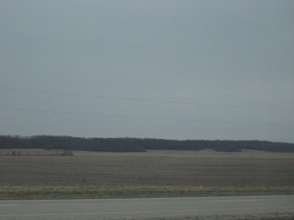 overcast sky above a wide, empty field with a treeline in the distance