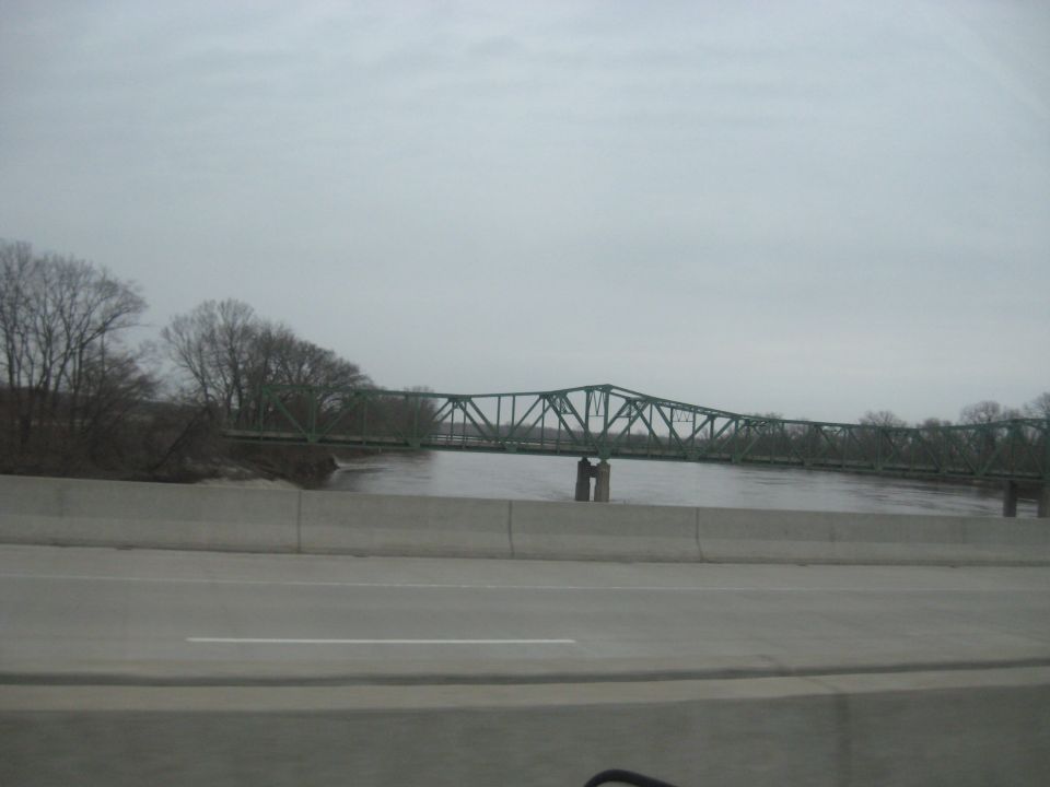 Green truss bridge over a wide river, seen from a highway