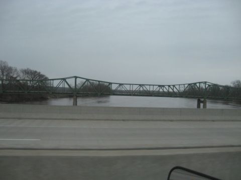 1978 Ford Bronco - A long, green truss bridge spans a river, with trees and a cloudy sky visible in the background.