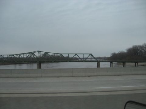 1978 Ford Bronco - A long, green truss bridge spans a river, with trees visible on the far bank under an overcast sky.