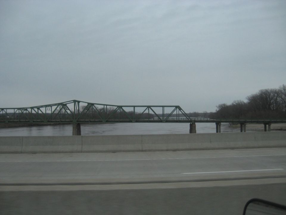 Green truss bridge over a wide river under a cloudy sky