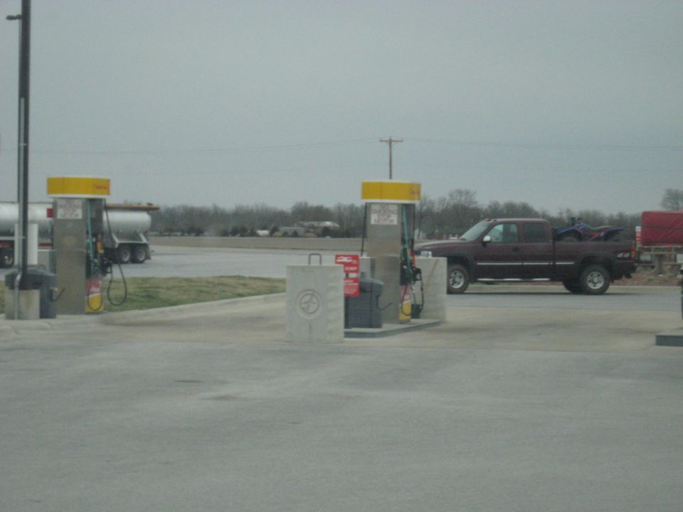 Maroon pickup truck with ATV in bed parked at gas station