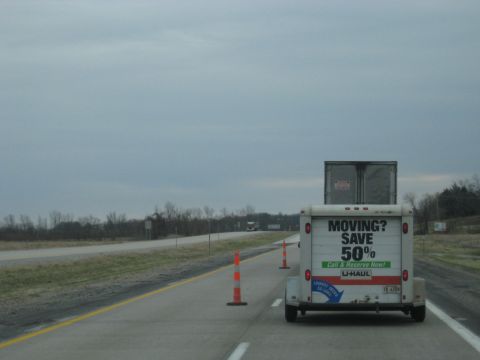 1978 Ford Bronco - A U-Haul trailer and semi-truck are traveling on a highway under an overcast sky.