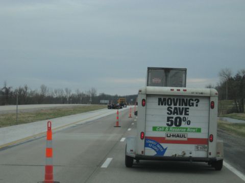 1978 Ford Bronco - A U-Haul trailer is seen from behind on a highway, with traffic cones and other vehicles ahead.