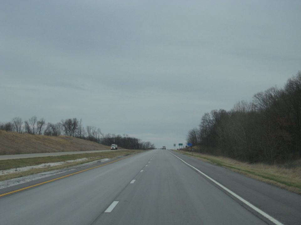 Highway driving scene with two vehicles visible in the distance under an overcast sky