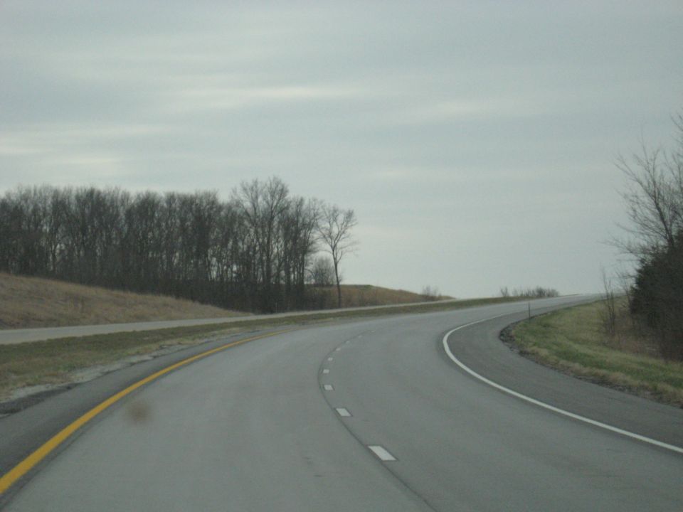 empty highway curving to the right with trees and a cloudy sky