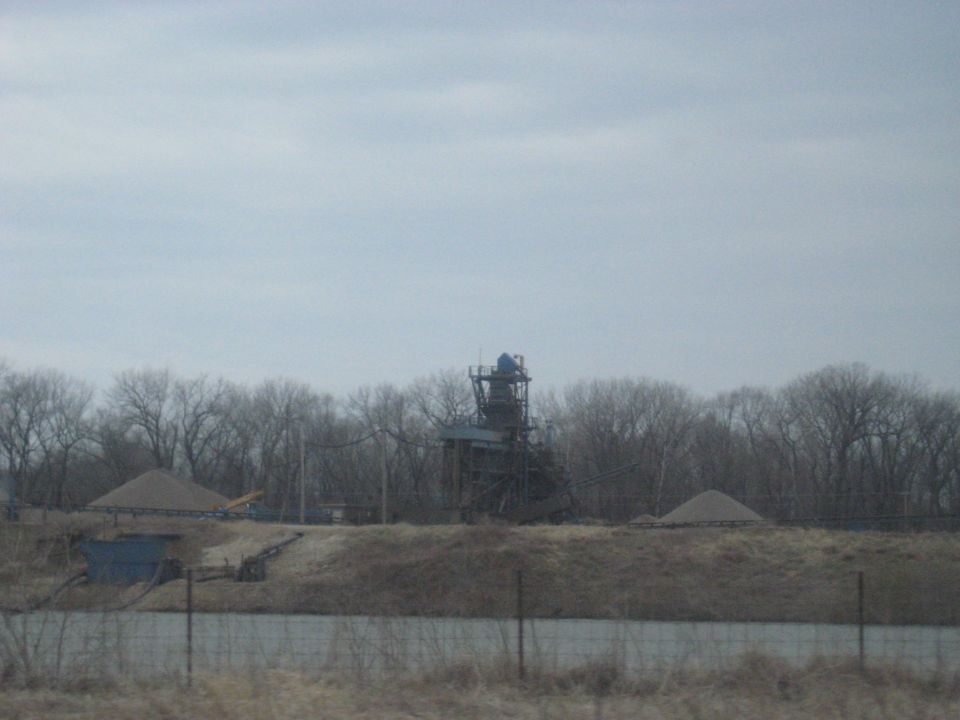 Industrial gravel processing plant with piles of gravel and bare trees under a cloudy sky
