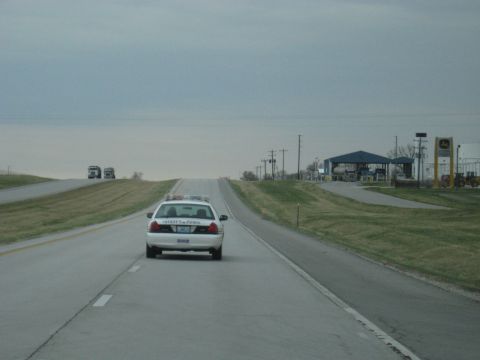 1978 Ford Bronco - A police car is seen from behind on a highway under an overcast sky.