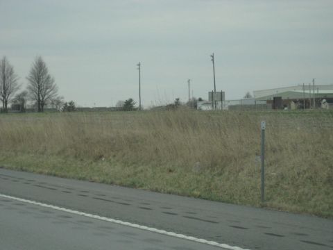 1978 Ford Bronco - A wide view of a rural landscape with a road in the foreground and buildings on the horizon.