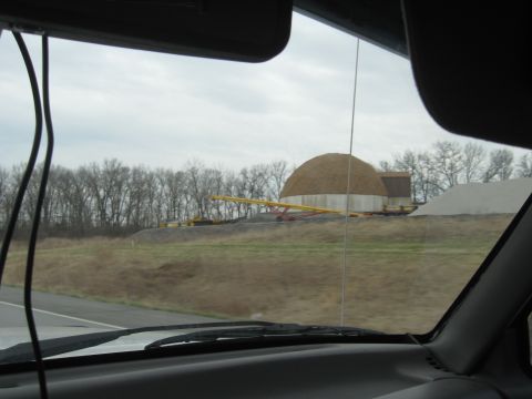 1978 Ford Bronco - Driving past an industrial site with a large dome structure and material storage piles under a cloudy sky.