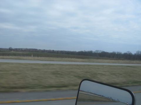 1978 Ford Bronco - A cloudy day view of a highway and surrounding fields, captured from the perspective of a side mirror.