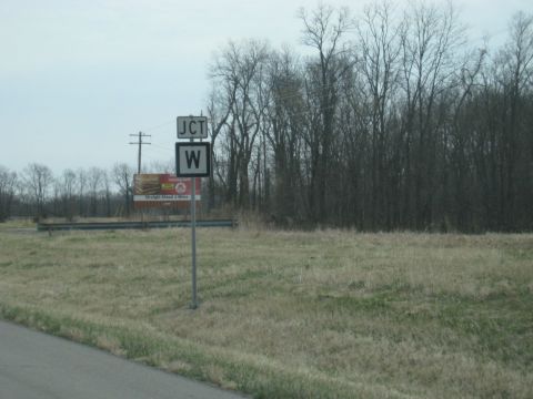 1978 Ford Bronco - Roadside view of a junction sign and a billboard, with a line of trees in the distance.
