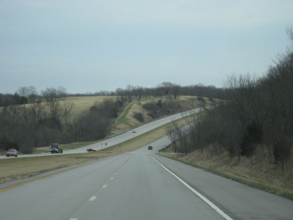 Highway scene with a red car, a truck, and two other cars visible on a cloudy day