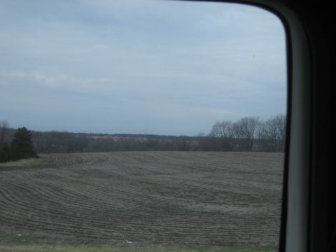1978 Ford Bronco - A view of a tilled field under a cloudy sky, seen through a vehicle window.