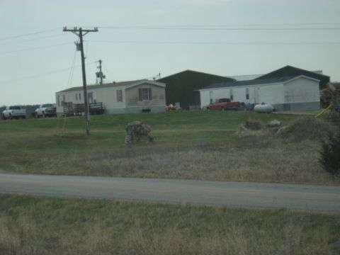 1978 Ford Bronco - Several vehicles are parked in front of mobile homes and a large building on a rural property.
