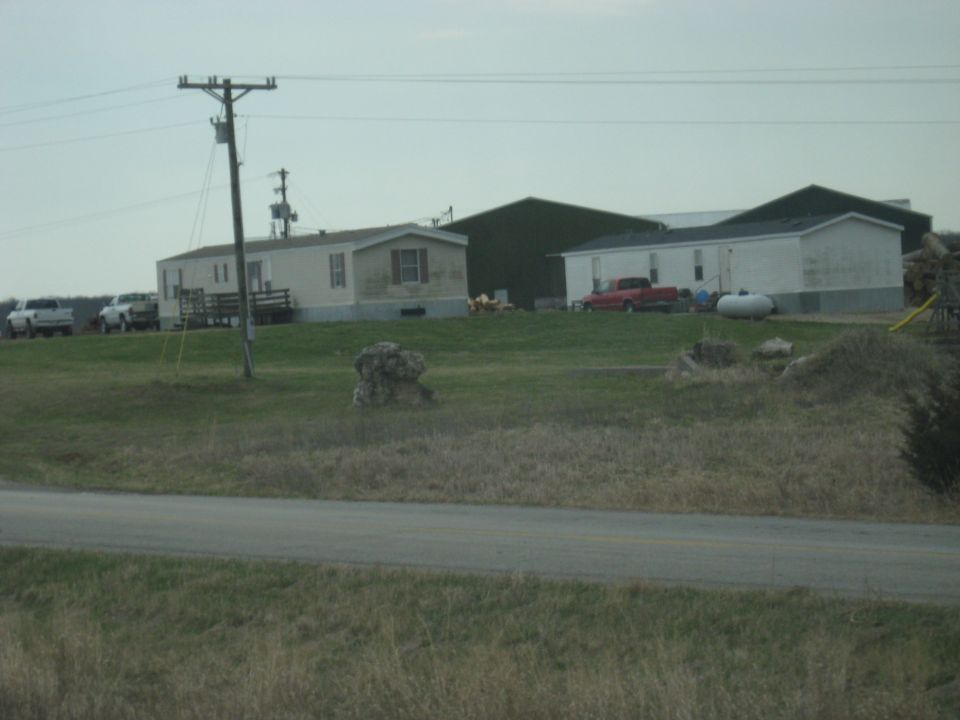 Farm scene with mobile homes, a red pickup truck, and two white pickup trucks parked in front of a building