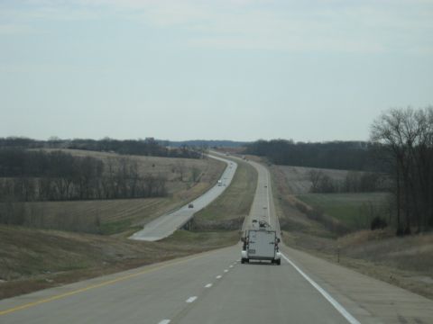 1978 Ford Bronco - A white cargo trailer travels down a long, straight highway through a rural landscape.