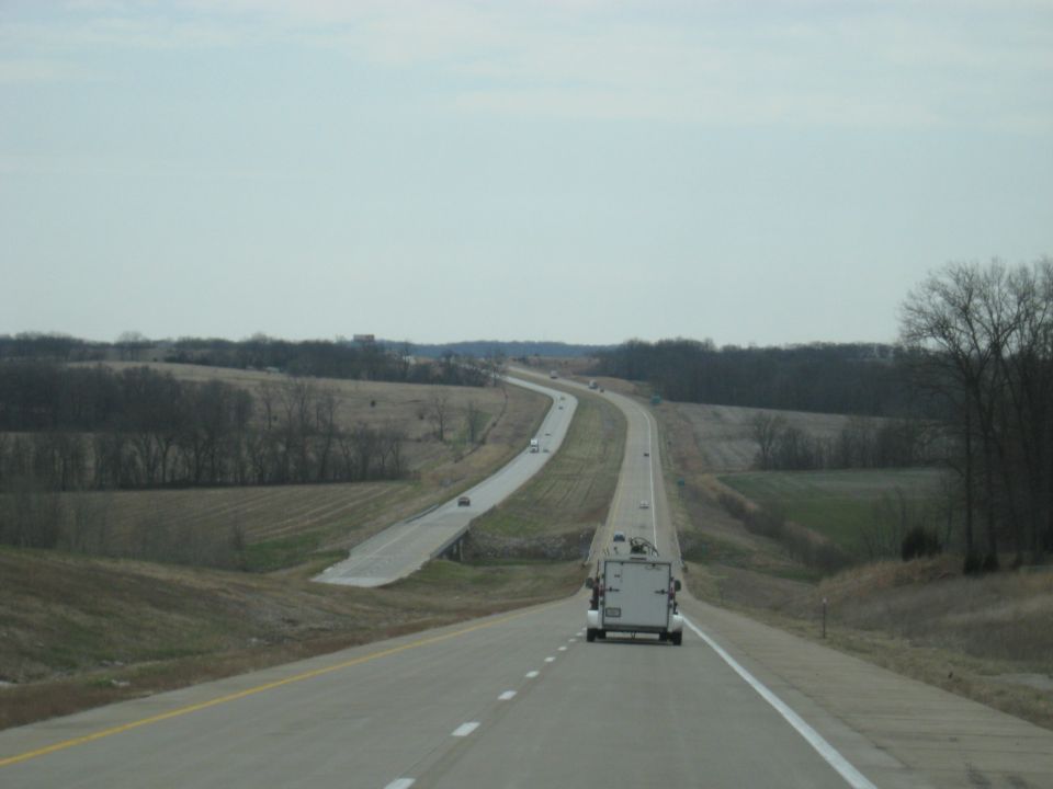 White cargo trailer with equipment on top, viewed from behind on a highway