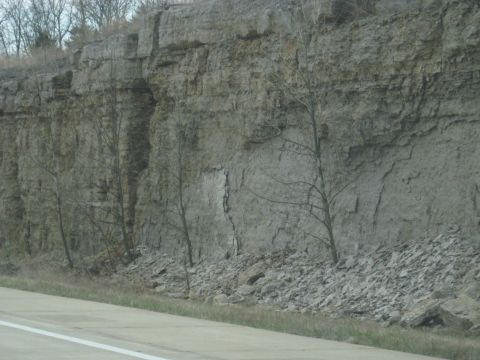 1978 Ford Bronco - A rocky cliff face with fallen debris and sparse vegetation lines the side of a road.