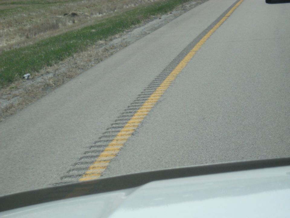 View from inside a vehicle looking at a highway lane with a yellow dashed line and rumble strip