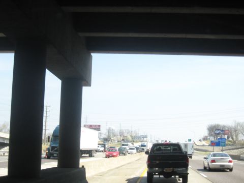 1978 Ford Bronco - Traffic moves along a highway beneath a large concrete overpass, with various vehicles including a black pickup truck and a semi-trailer vi…