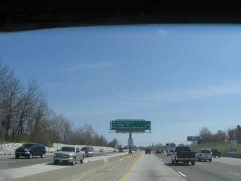 1978 Ford Bronco - Multiple vehicles travel on a highway under a bright blue sky with a directional sign overhead.