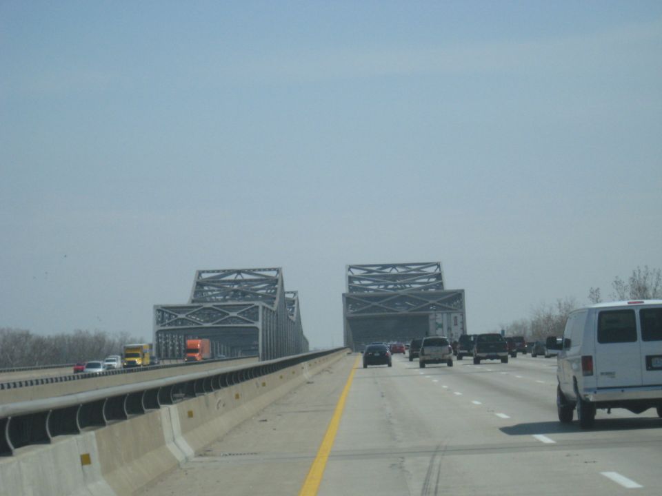 White van driving on a highway with a large bridge in the background