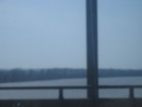 1978 Ford Bronco - A blurry, overcast day shows a distant tree line across a body of water, viewed from inside a vehicle.