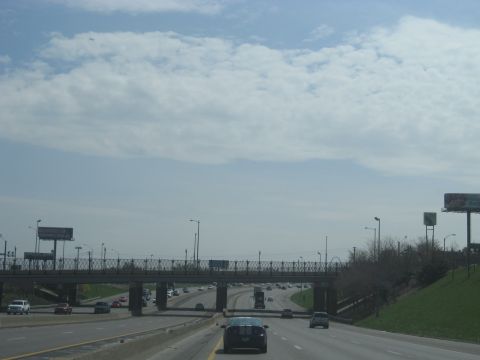 1978 Ford Bronco - A busy highway scene unfolds with multiple vehicles navigating under a pedestrian overpass, while billboards loom in the distance.