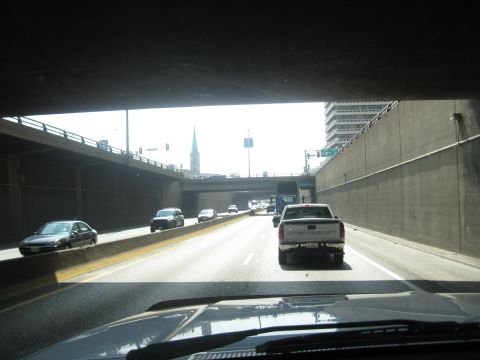 1978 Ford Bronco - A silver Chevrolet pickup truck travels down a highway under an overpass, with other vehicles visible in the distance.