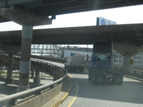 1978 Ford Bronco - Multiple trucks are seen on an elevated highway, passing under concrete overpasses and bridges.