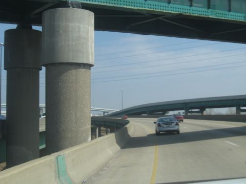 1978 Ford Bronco - Cars travel on a highway beneath large concrete bridge supports and a green metal overpass.