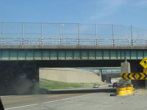 1978 Ford Bronco - Several cars travel on a highway beneath a large green bridge with a chain-link fence on top.