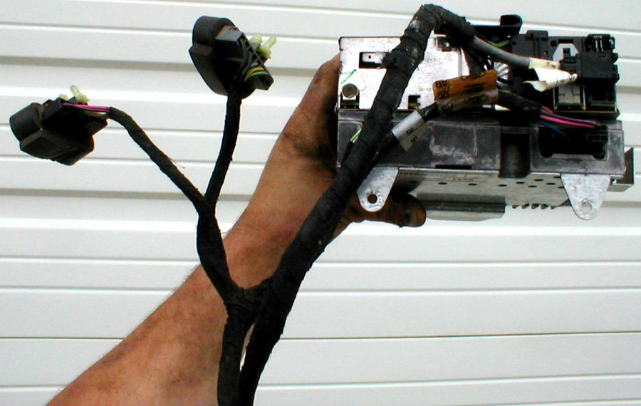 Hand holding a radio amplifier or module with attached wiring harness pigtails