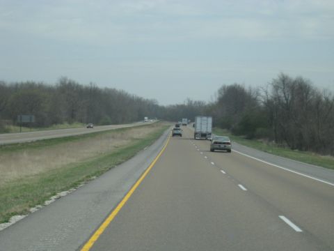 1978 Ford Bronco - Vehicles travel along a highway under an overcast sky, with trees lining the roadside.
