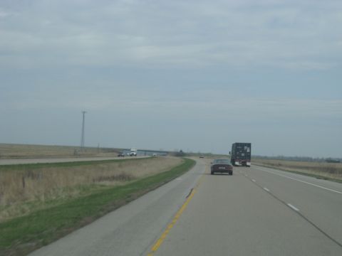1978 Ford Bronco - A red car travels down a highway, passing a large truck under an overcast sky.