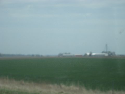 1978 Ford Bronco - Distant farm structures are visible across a green field on an overcast day.