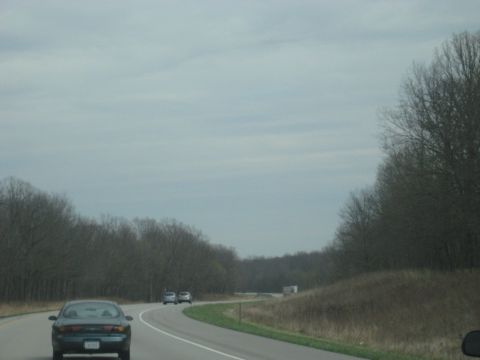 1978 Ford Bronco - Multiple vehicles travel along a highway bordered by trees under a cloudy sky.