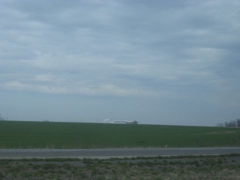 1978 Ford Bronco - Distant farm buildings are visible across a green field under a vast, cloudy sky.